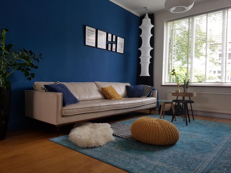 Акцентна стіна синього кольору, світлі меблі та жовті декоративні подушки та пуф