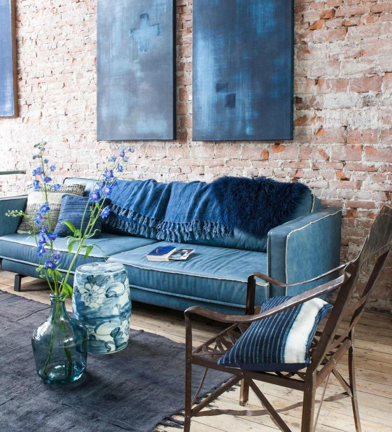 Синій оксамитовий диван з ковдрами на тлі цегляної стіни