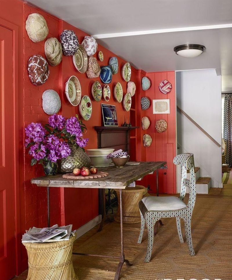 Червона стіна з колекцією декоративних тарілок відокремлює обідній куточок від робочого простору кухні